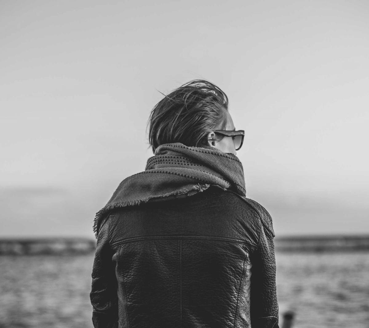 A person in a scarf and sunglasses looking out over the sea